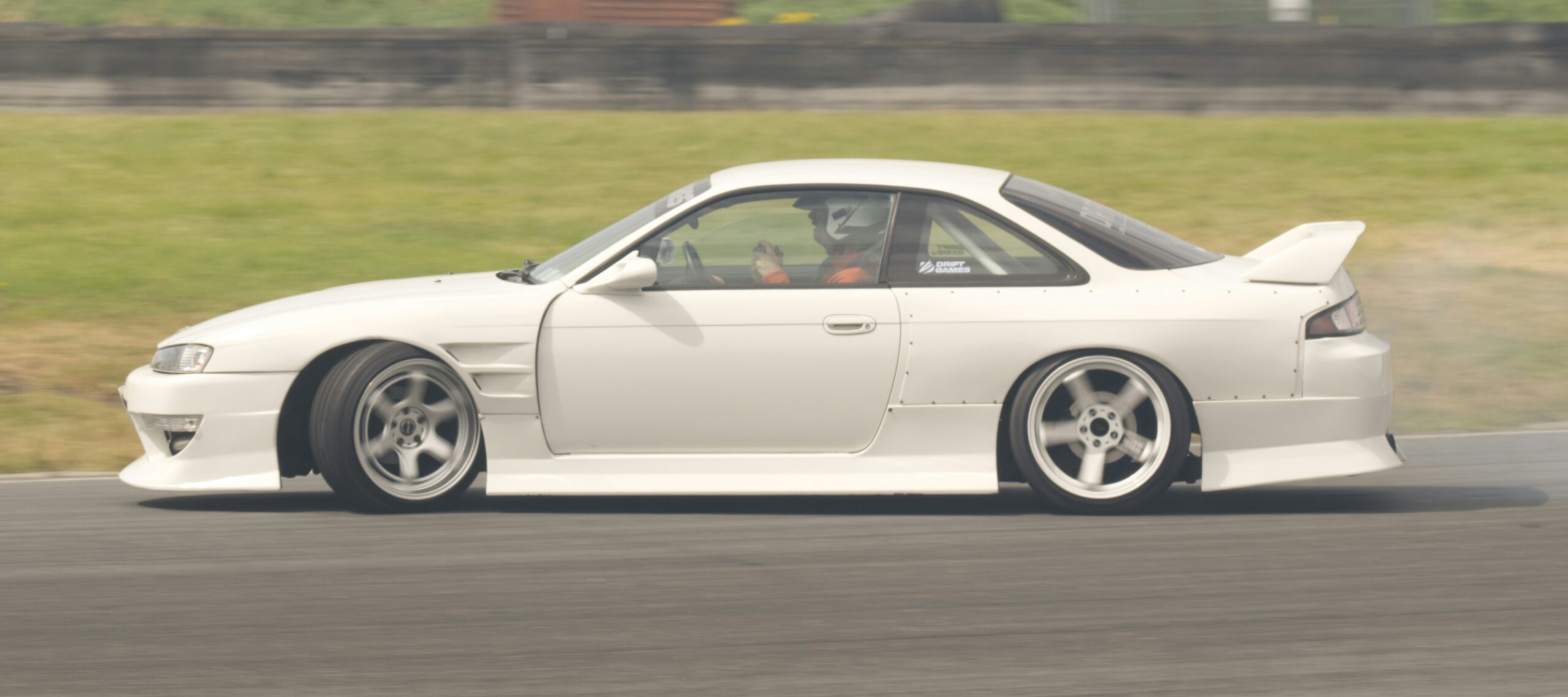 A white car is speeding around a racetrack.  By Kevin Dowling