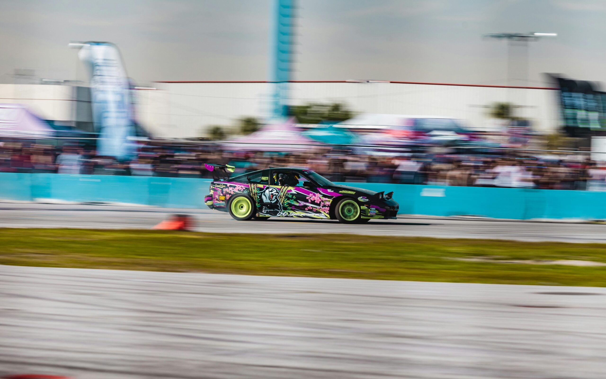 Blurred motion shot of a colorful car drifting fast on a racetrack during a lively racing event.