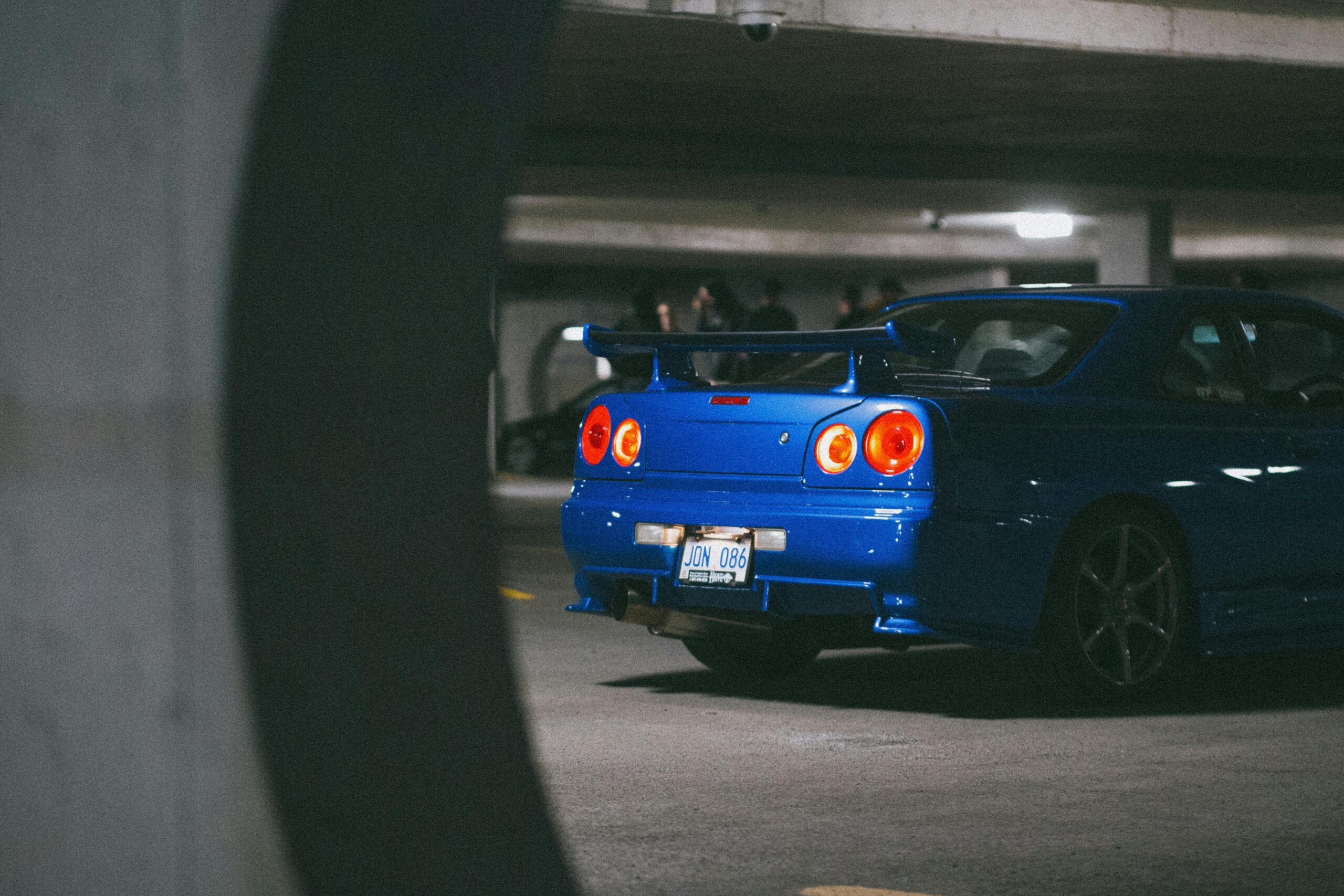 A blue Nissan Skyline GT-R parked in an underground garage, showcasing its sport design and tail lights.  By Erik Mclean