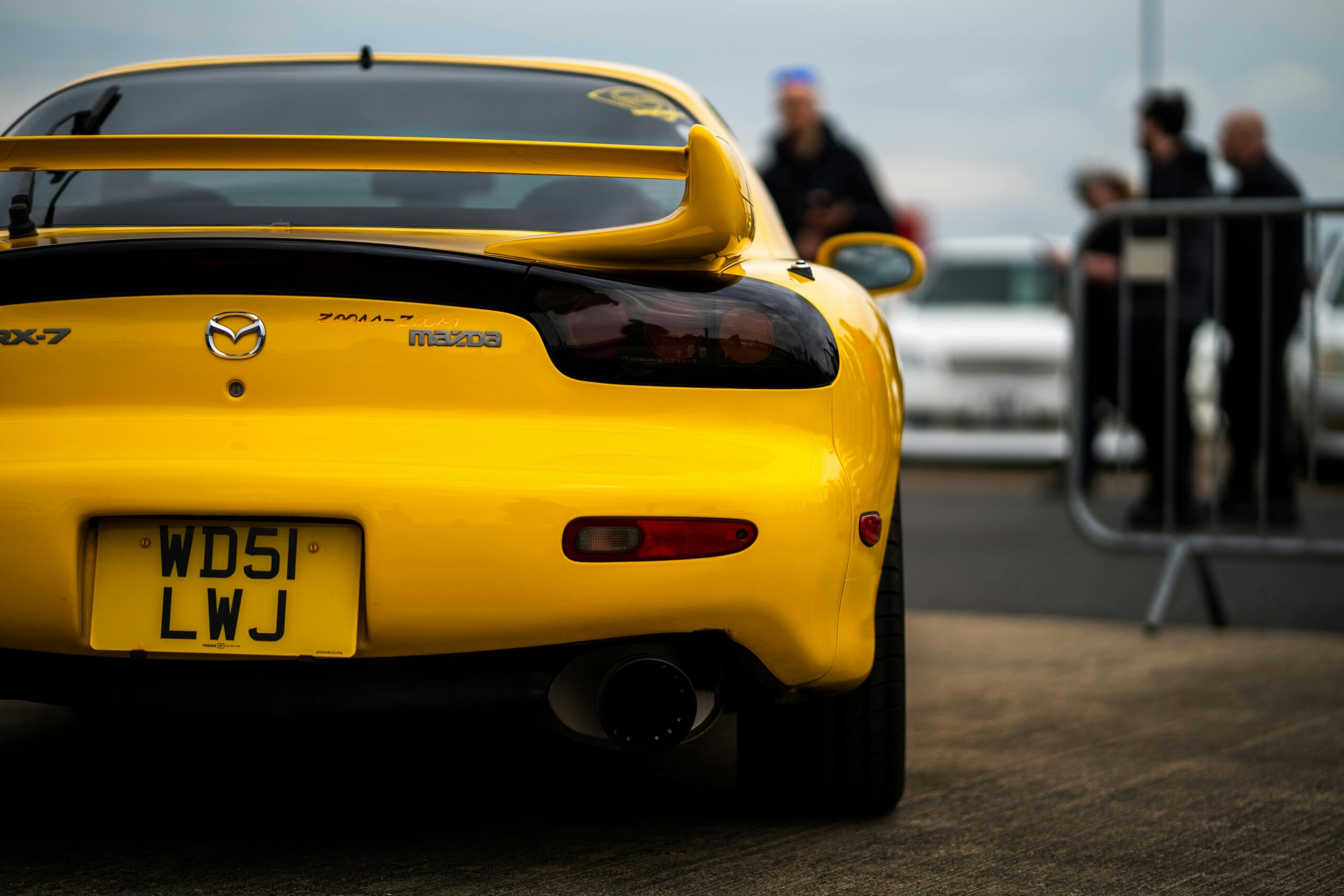 A vibrant yellow Mazda RX-7 showcased at Japfest 2025, with a focus on its sleek rear design and sporty aesthetics.